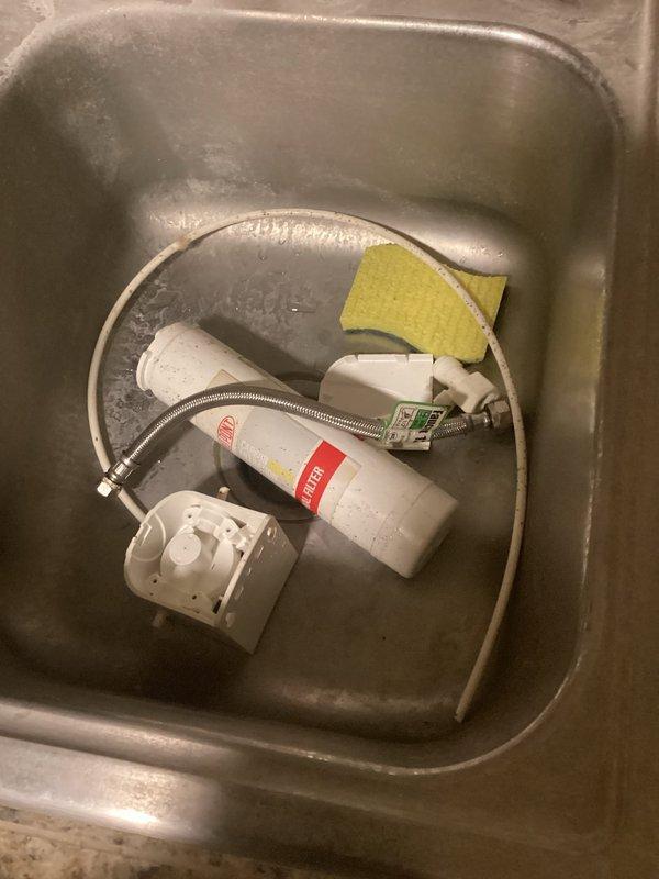 Diagnosed leak coming from single-stage RO system under kitchen sink. Found water pooling beneath the unit with visible droplets on PVC piping and staining on cabinet wall. Removed the faulty RO system including filter cartridge and disconnected associated supply lines to resolve the immediate leak issue.