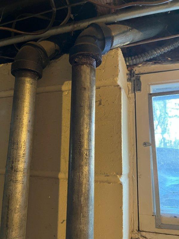 Attended property to diagnose basement leak located at galvanized pipe junction below kitchen sink where it connects to main sewer line. Visual inspection confirmed significant corrosion and rust at threaded connections of cast iron elbow fitting joining vertical and horizontal pipes. Conducted assessment and sold replacement estimate as existing galvanized piping has rusted through, requiring complete replacement. Scheduled return visit to perform full pipe replacement.
