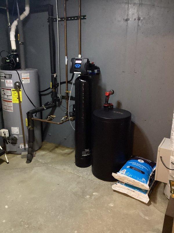 Performed comprehensive plumbing inspection of residential property, examining water treatment system consisting of dual black tanks and water softener setup with adequate salt supply. Inspected water heater for proper connections and safety compliance, and evaluated bathroom fixtures including sink, faucet, and drain for functionality and condition, with all components appearing to be in good working order.