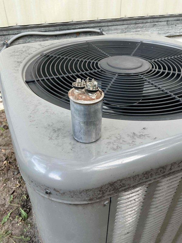 Responded to no-cooling complaint on 5-year-old Rheem AC system. Diagnosed failed capacitor (visibly bubbled on top) which prevented fan motor operation. Replaced capacitor, restoring proper system function and cooling. Customer reported neighborhood power fluctuations likely contributed to component failure.