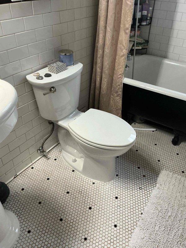 Successfully installed new elongated toilet in bathroom per estimate, connecting the braided stainless steel water supply line to the existing shutoff valve. Completed installation in bathroom with white subway tile walls and hexagonal tile flooring.