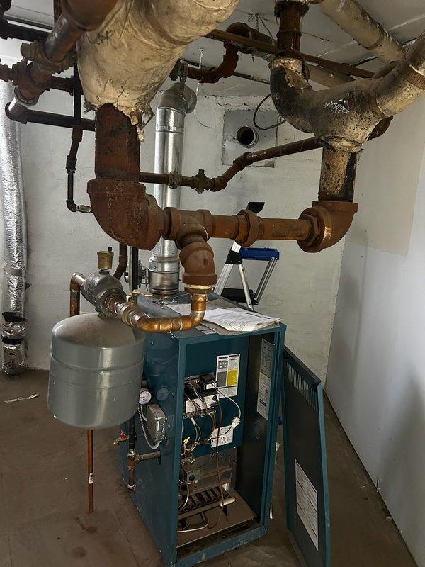 Responded to no-heat callback on residential boiler system. Upon arrival, confirmed boiler was non-operational due to blocked chimney flue preventing proper venting. Inspected venting system and documented obstructed condition with photos showing the boiler unit, associated piping infrastructure, and vertical flue pipe configuration. Customer had already arranged for chimney service contractors to address the blockage. Verified boiler safety controls were functioning properly and system was in lockout mode as designed due to inadequate draft conditions. Explained situation to customer and confirmed chimney professionals would resolve the venting obstruction to restore safe operation.