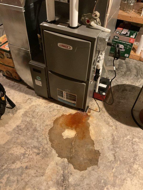 Diagnosed water leakage from 2-year-old Lennox furnace that customer reported has been occurring since installation. Inspection revealed a cracked cold end header box around the screws and trap connection points due to overtightening during original installation. Documented damage with photos showing water damage on concrete floor beneath unit. Submitted warranty part order form for replacement cold end header box.